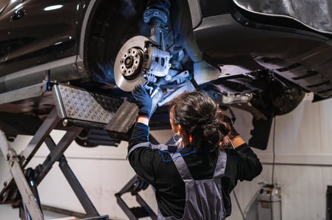 Female mechanic working under a car on hydraulic lift inspecting brakes