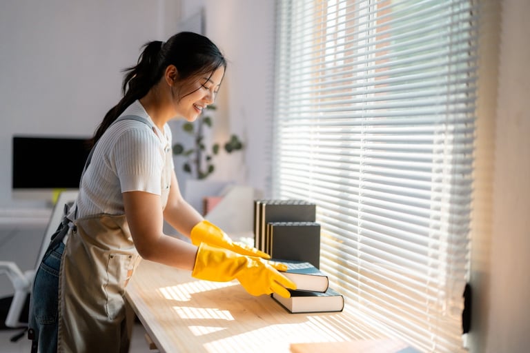 Cheerful housekeeper cleaning wooden table with yellow gloves